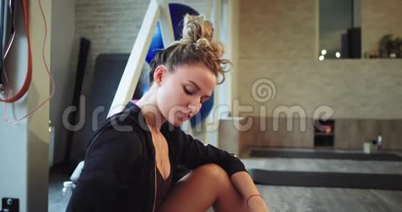 一个漂亮的金发美女在有氧运动后一边坐着一边喝着塑料瓶里的水又累又渴视频的预览图