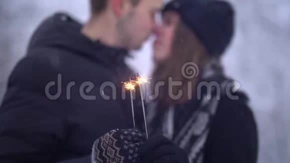 模糊的数字年轻的男人和女人接吻的背景下燃烧的火花在白雪覆盖的公园冬季视频的预览图