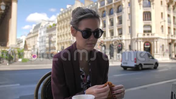 迷人的巴黎女性在巴黎市中心的一家街边咖啡馆吃牛角面包在一个视频的预览图