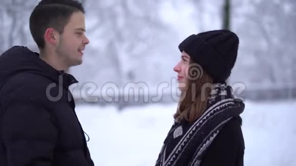 肖像可爱的年轻女人和男人在冬天的公园里亲吻下飘落的雪恋爱中的幸福夫妻享受在一起的时光视频的预览图