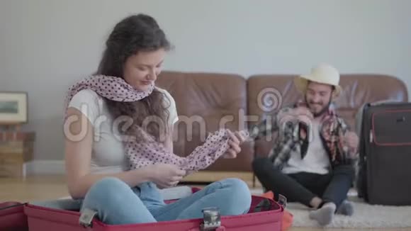 坐在手提箱里的可爱女人和坐在沙发边准备打包的胡子男人视频的预览图