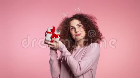 年轻可爱的女孩微笑着拿着礼物盒在粉红色的工作室背景视频的预览图