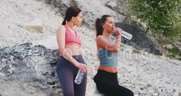 两位口渴的女士在大自然中进行了一次艰苦的锻炼后在一块大石头旁边停了下来并用塑料瓶喝水视频的预览图