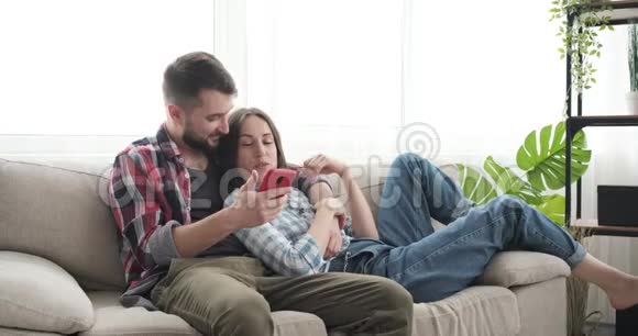 情侣在沙发上用手机浏览社交媒体视频的预览图