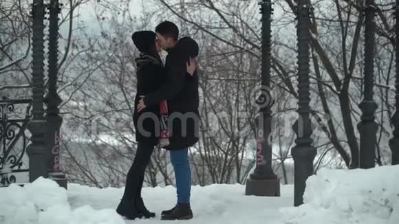 在白雪覆盖的冬季公园里美丽的年轻女子和男人热情地接吻快乐的情侣享受时光视频的预览图