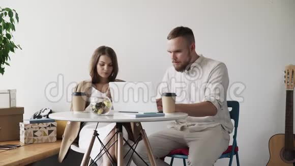 两个年轻人在咖啡馆里用笔记本电脑和电话工作休息时男人和女人坐在桌旁的咖啡馆里视频的预览图