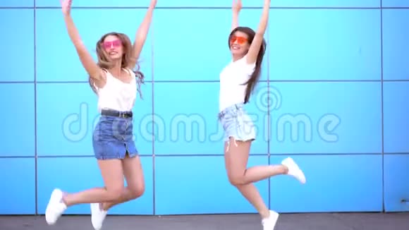 两个年轻的时髦女人在蓝墙上跳着笑视频的预览图