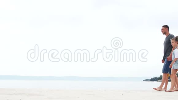 一个年轻人和两个孩子一个男孩和一个女孩坐在海边的白沙上暑假父亲天视频的预览图