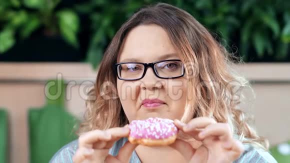 特写肖像微笑的胖女人嚼着美味的甜甜圈摆姿势看着镜头视频的预览图