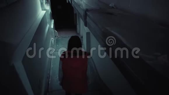 年轻的黑发女人穿着红色无袖夹克在黑暗中走着长长的楼梯视频的预览图
