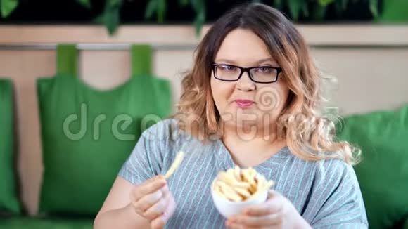 快乐胖女人吃着开胃的炸薯条摆姿势看镜头的画像视频的预览图