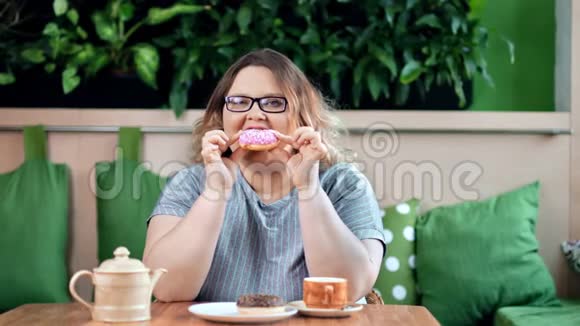 爱笑的胖女人喜欢吃美味可口的甜甜圈看着镜头视频的预览图