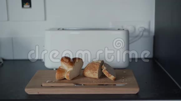 新鲜切片面包在木切割板上与模糊的白色烤面包机关门视频的预览图