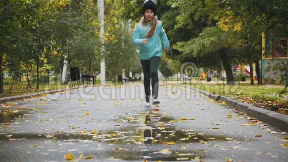 秋雨过后女孩在公园的水坑里玩耍和跳跃秋季雨天户外活动幼儿孩子视频的预览图
