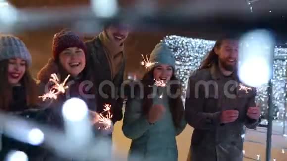 在大雪纷飞的冬夜朋友们在节日的照明隧道里与火花漫步玩得很开心快乐的人群视频的预览图