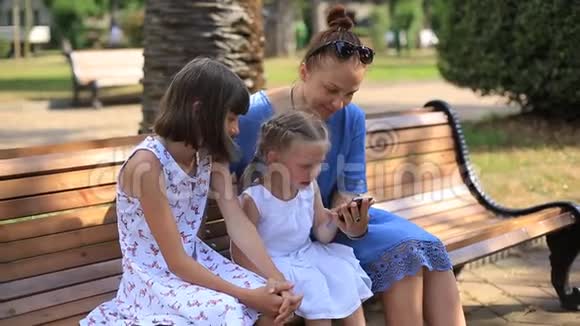 一个女人和女儿坐在公园里通过智能手机上的视频通话与朋友交流视频的预览图