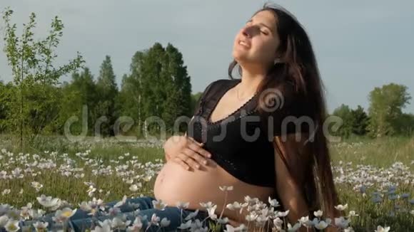 年轻的孕妇坐在花田里视频的预览图