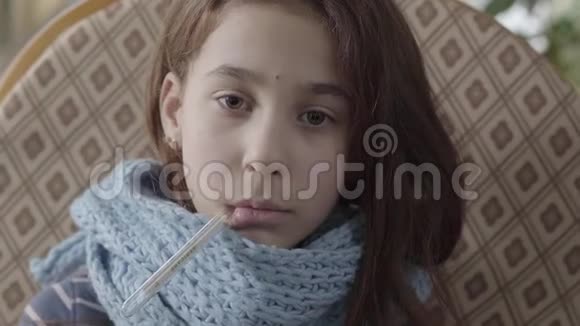 十几岁的女孩裹着温暖的围巾嘴里拿着温度计测量温度的肖像女孩视频的预览图