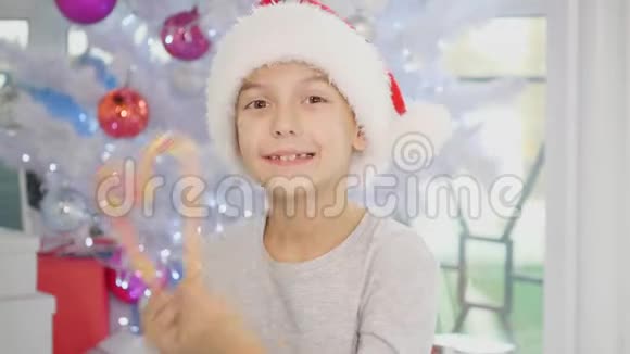 4k视频圣诞男孩坐在圣诞树附近玩糖果透过一根甘蔗心视频的预览图