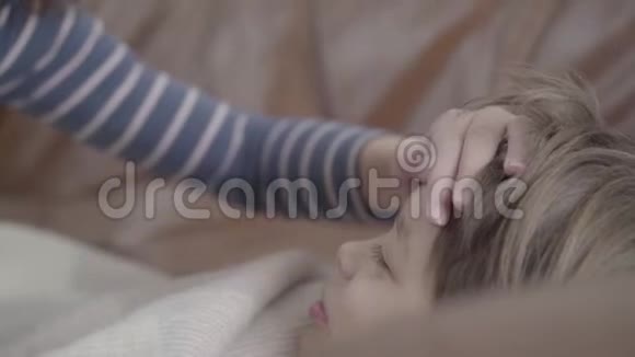 女人的手躺在一个生病的小男孩的额头上紧紧地那家伙躺在床上裹着毯子视频的预览图