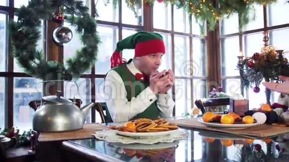 圣诞背景下坐在桌边的一只拿着杯子的雄性精灵视频的预览图