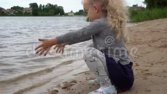 四岁的贪玩女孩坐在湖水边用沙子付钱万向节运动视频的预览图