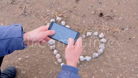男人用手机双手特写在沙滩上用贝壳拍心视频的预览图