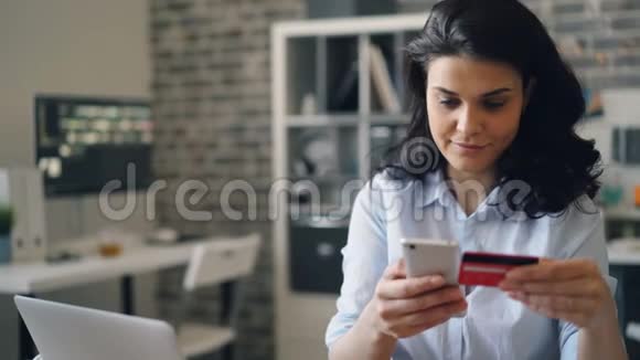 快乐的女孩在办公室用智能手机用信用卡在线购物视频的预览图