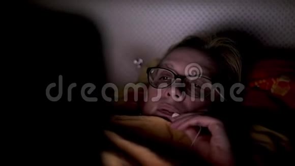 那个女人脸被笔记本显示器照亮女孩躺在毯子下面的床上看着屏幕视频的预览图
