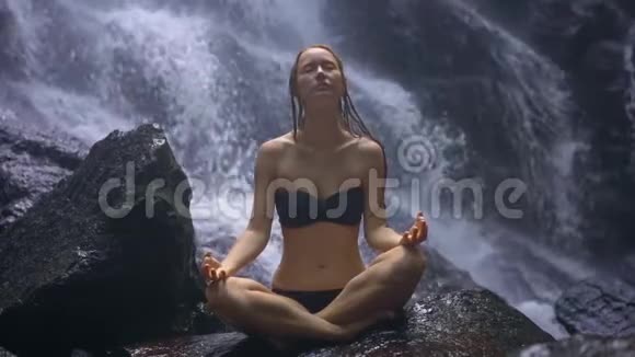 年轻女子坐在岩石上身后溅起瀑布视频的预览图
