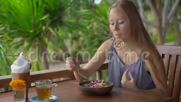 一个在热带咖啡馆里的年轻女人吃健康的素食沙拉素食概念视频的预览图