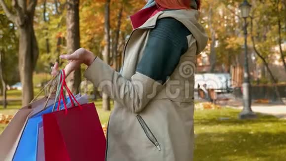 一个长着狐臭头发的女孩站在公园里用多种颜色的纸袋买东西视频的预览图