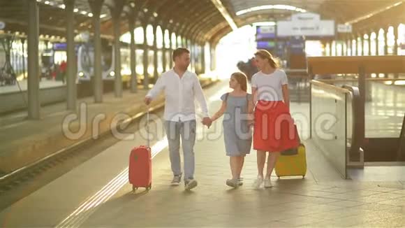 有女儿的年轻夫妇休假家庭步行在火车站平台与手提箱快乐视频的预览图
