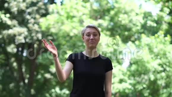 在斯洛莫的一个绿色公园里一个快乐的金发女人挥手微笑视频的预览图