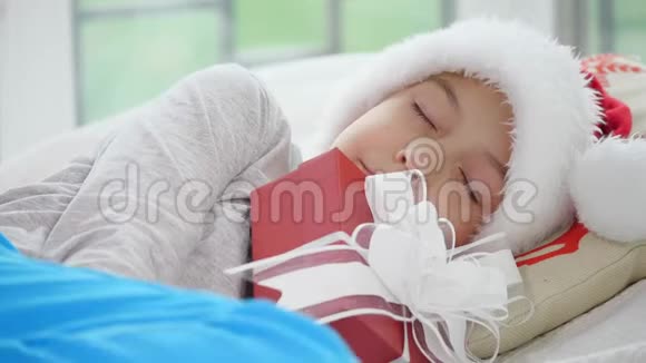 可爱的视频小男孩戴着圣诞帽睡在圣诞礼物视频的预览图