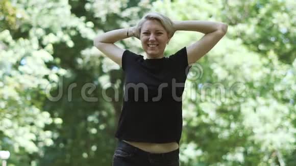 快乐的金发女人在闷热的公园里笑着举起双手视频的预览图