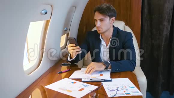 年轻英俊的首席银行家主任商人使用智能手机在飞机上飞行成功的业务视频的预览图