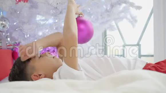 孩子躺在圣诞树下玩粉色球的视频视频的预览图