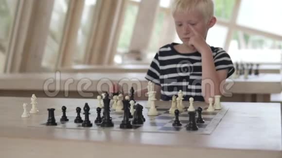 这个男孩下棋孩子坐在宽敞明亮的国际象棋俱乐部里视频的预览图