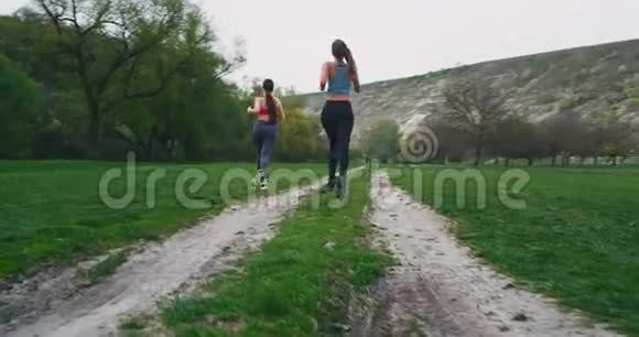 两位运动型女士在一个美丽的山景中奔跑在一个绿色的田野里视频的预览图