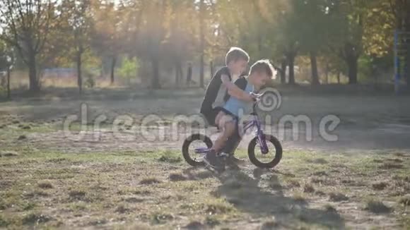 这个男孩和弟弟在夏天阳光明媚的天气里骑着摩托车在公园里玩心情很好视频的预览图