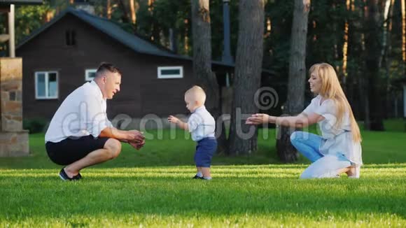 婴儿亲吻父亲快乐的小家庭在院子里和他们1岁的儿子玩耍视频的预览图