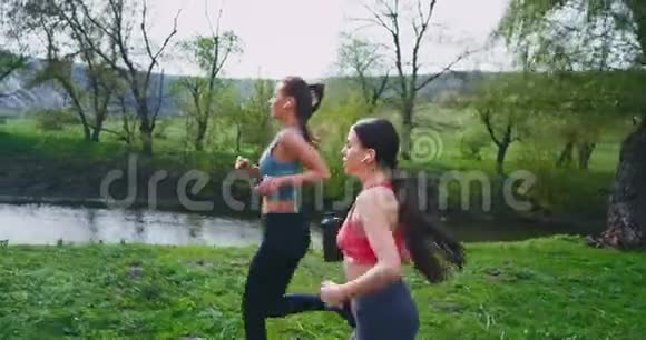 两位女士配备了健身器材手里拿着一瓶水和电话在大自然中穿过绿色的田野视频的预览图