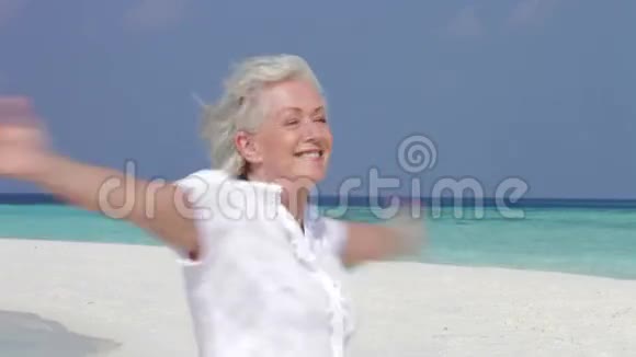 在美丽的海滩上伸展双臂的老年妇女视频的预览图