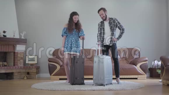 快乐的卷发女孩和留胡子的男人在旅行前收拾好了手提箱坐在他们身上年轻家庭视频的预览图