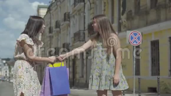 两个可爱的时尚年轻女人拿着购物袋把她们拉到街上的两边购物概念视频的预览图