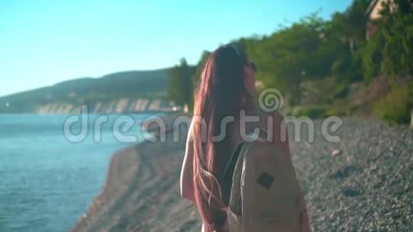 一个漂亮的女孩穿着红色的一件泳衣和眼镜沿着海滨散步肩膀上有一个米色的背包视频的预览图