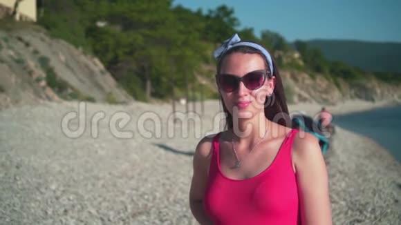 一个穿着红色的一件泳衣和眼镜的漂亮女孩站在海滨微笑着视频的预览图
