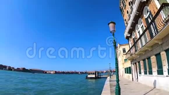 在意大利威尼斯阳光明媚的一天从池塘边的城市街道观看船只视频的预览图