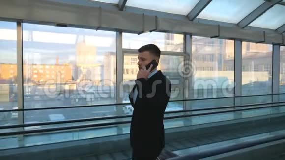自信的商人带着行李穿过候机楼的玻璃大厅打电话成功视频的预览图